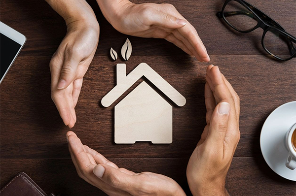 Hands of a couple protecting their house on wooden background